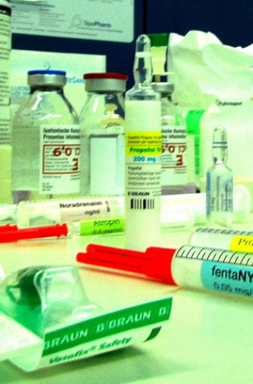Zusammenstellung von Medikamenten für die Narkose: Im Fokus eine Ampulle „Propofol“ (200 mg), flankiert von aufgezogenen Spritzen mit „fentaNYL“ und „Atropin“ sowie Infusionsflaschen im Hintergrund.