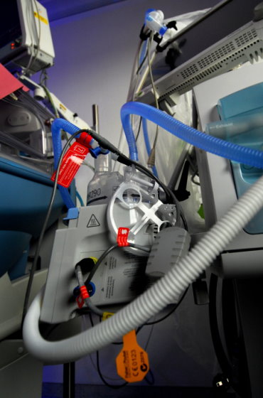 Detailaufnahme eines Atemgasbefeuchters (Fisher & Paykel) mit angeschlossenen Beatmungsschläuchen und Kabelsystemen an einem medizinischen Gerätewagen.