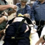 Mehrere medizinische Fachkräfte behandeln einen auf einer Trage liegenden Patienten, der mit Gurten gesichert ist, während Geräte und Kabel angeschlossen werden.